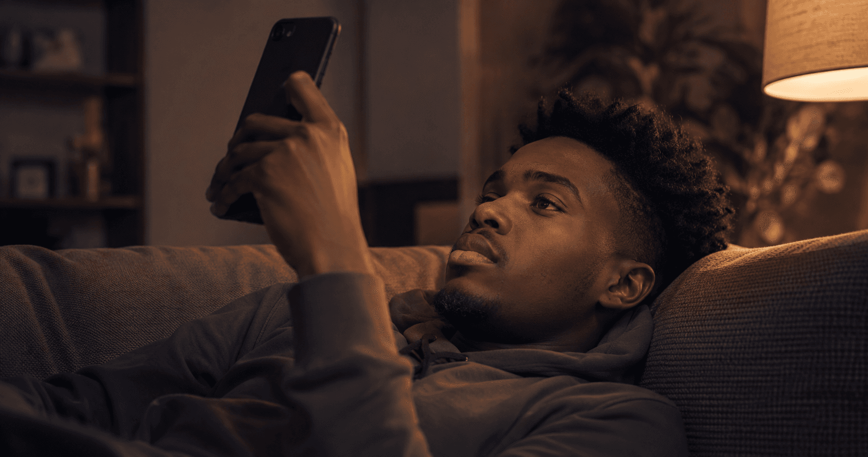 Young adult pausing mid-scroll on their phone while lying on  a couch, representing the moment of noticing time spent  scrolling without much to show for it