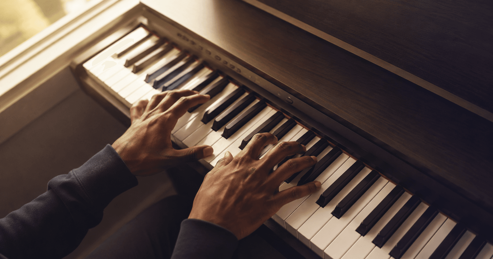 Close-up of hands positioned correctly on piano keys in a  warmly lit room.