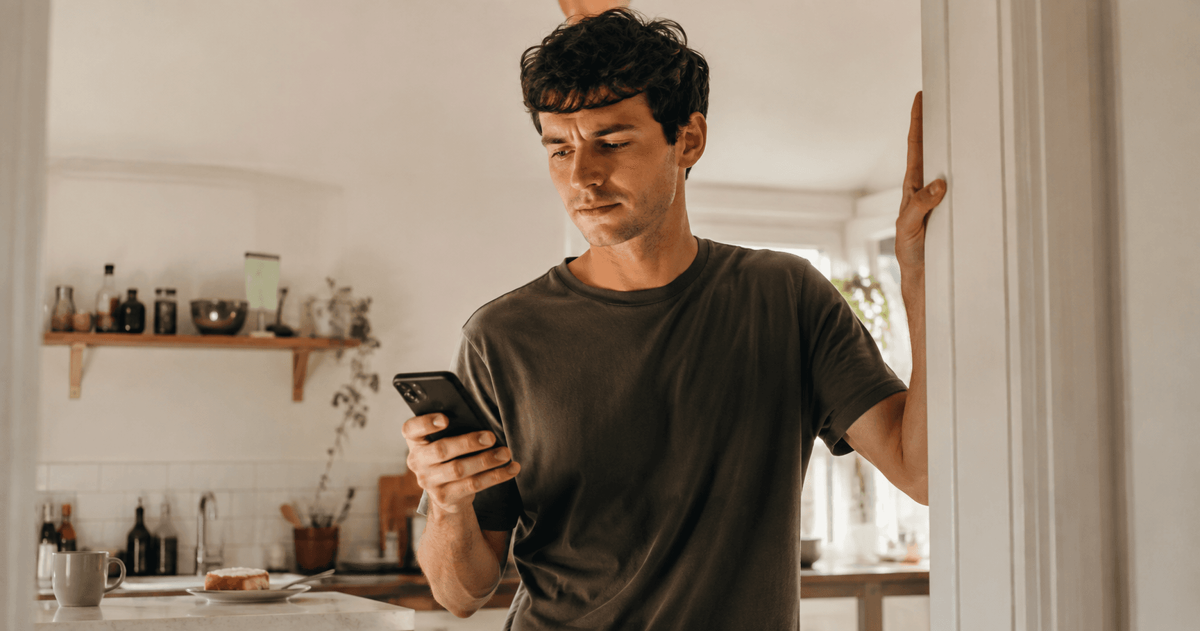 A warm editorial kitchen scene captures the moment of hesitation, with the subject visibly aware of the urge to reach for the phone.